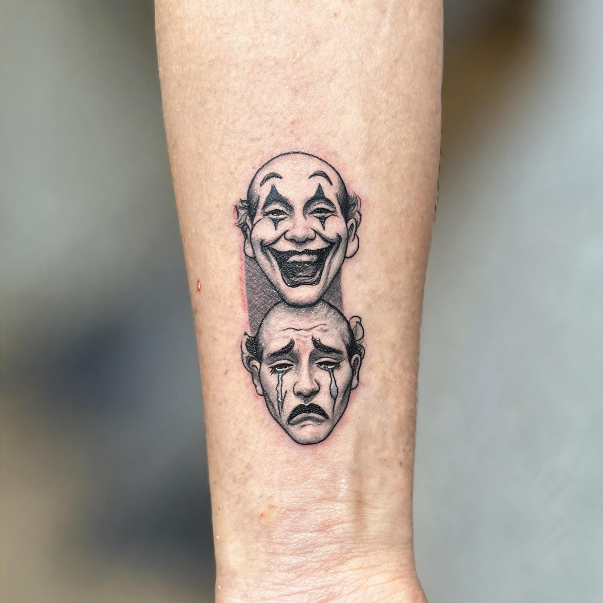 Black and grey laugh now cry later tattoo image on an inner forearm, shown on real skin against a neutral background.