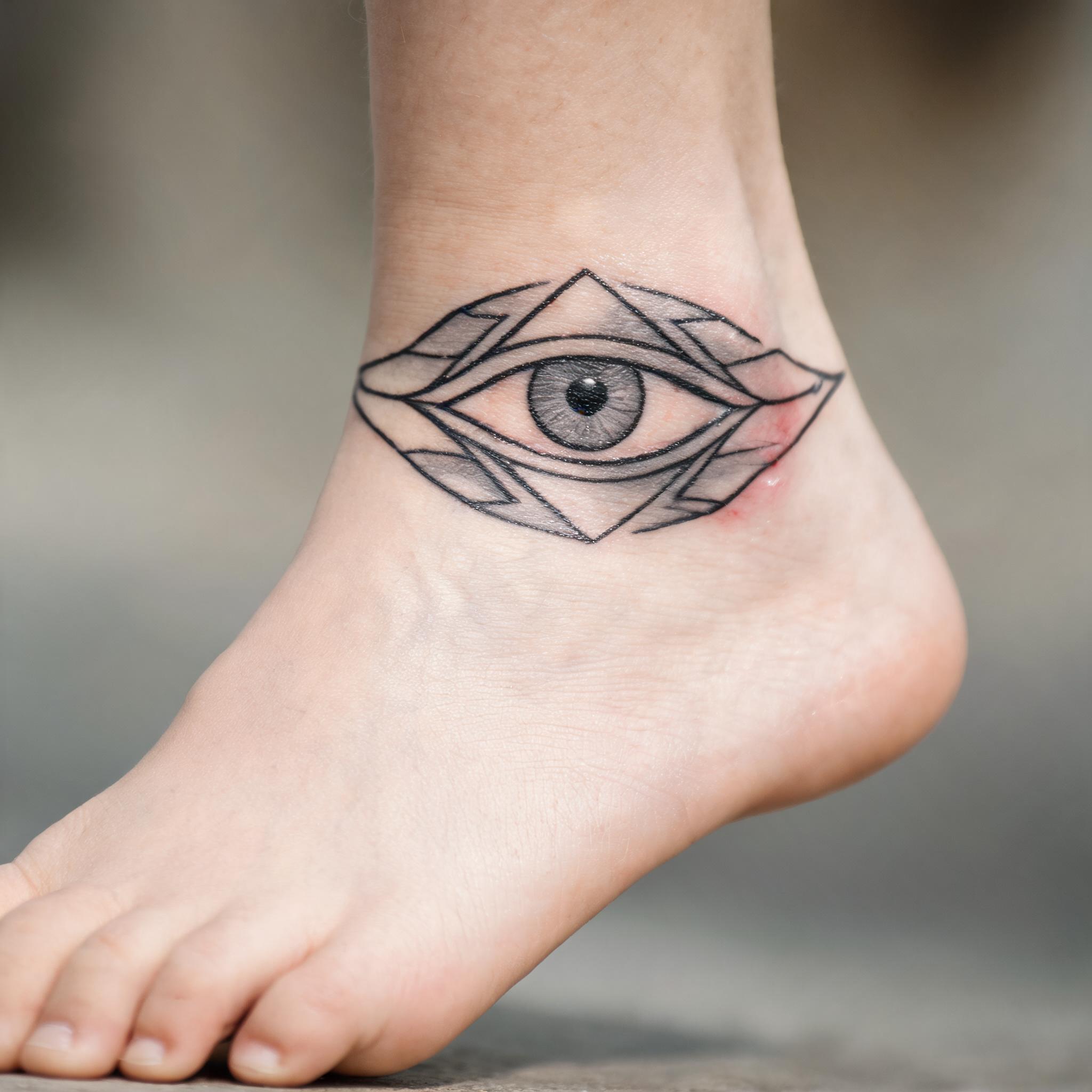 Minimalist black-and-grey tattoo image of a mystic images tattoo co design wrapping an ankle, shown on skin against a white background.