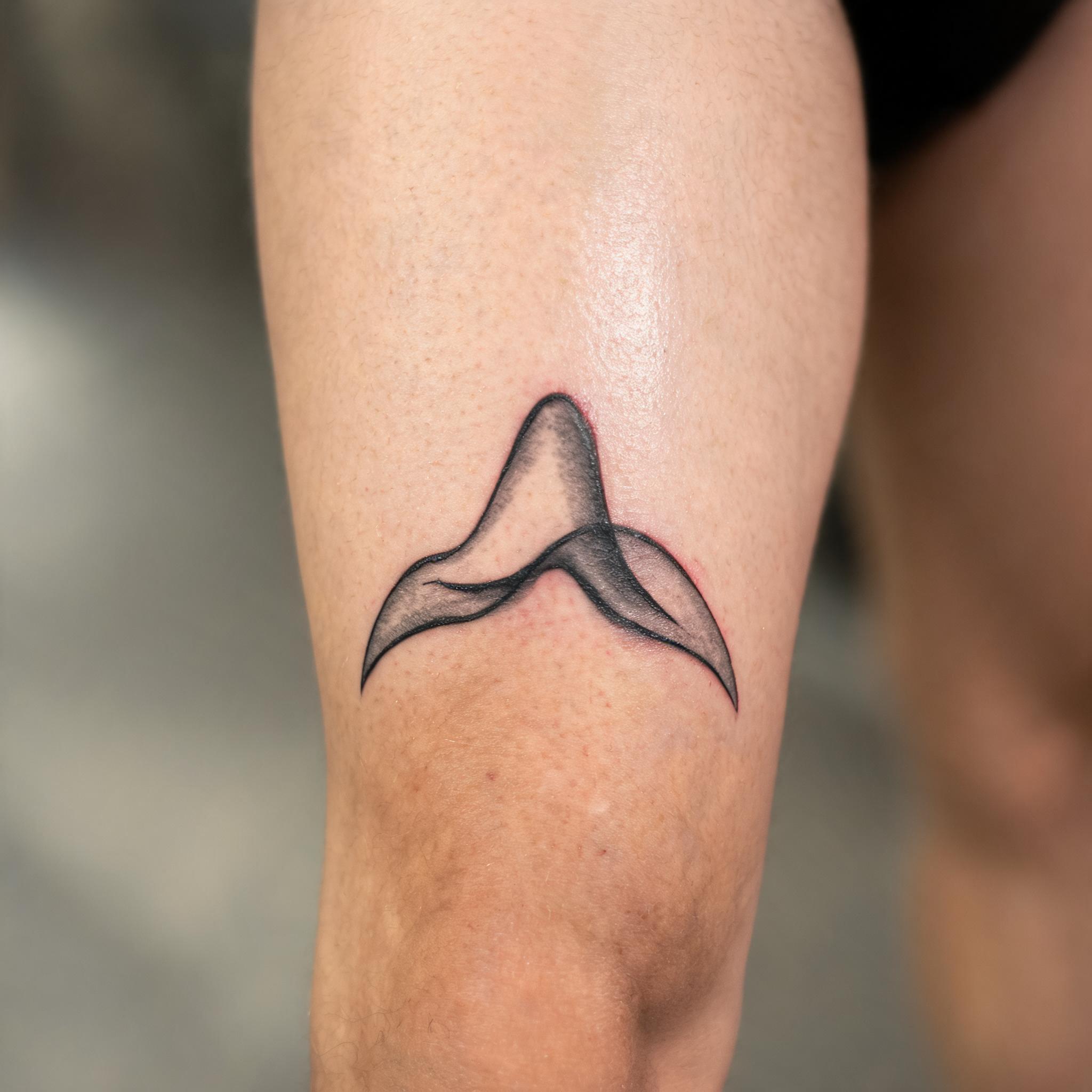 A minimalist tattoo image for men on the front thigh, shown in black and grey ink against real skin in a clean editorial photograph.