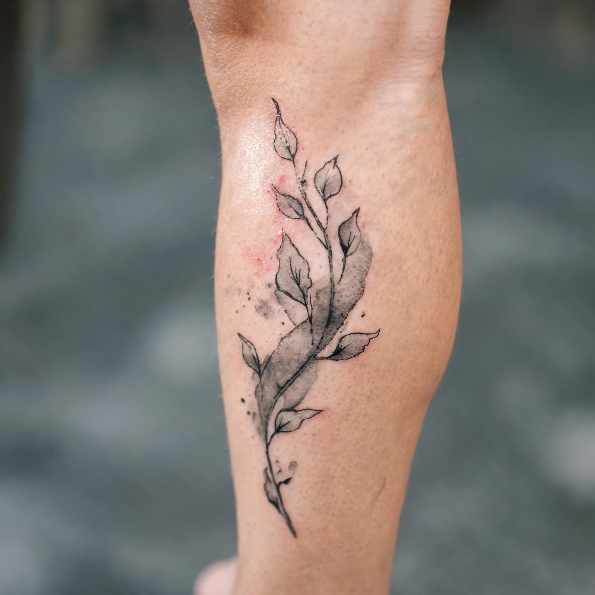 A watercolor-style true image tattoo in black and grey ink shown on the calf of a person's lower leg against a neutral background.