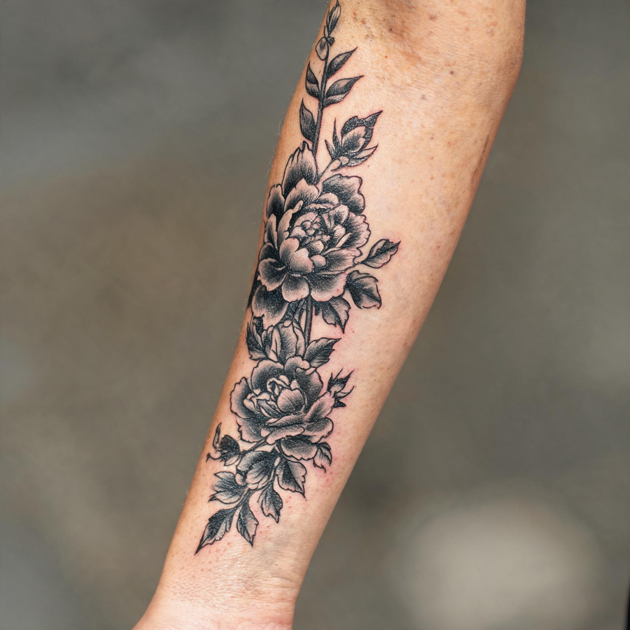 Blackwork floral tattoo on an outer forearm, shown on skin against a clean neutral background in a tattoo photograph.