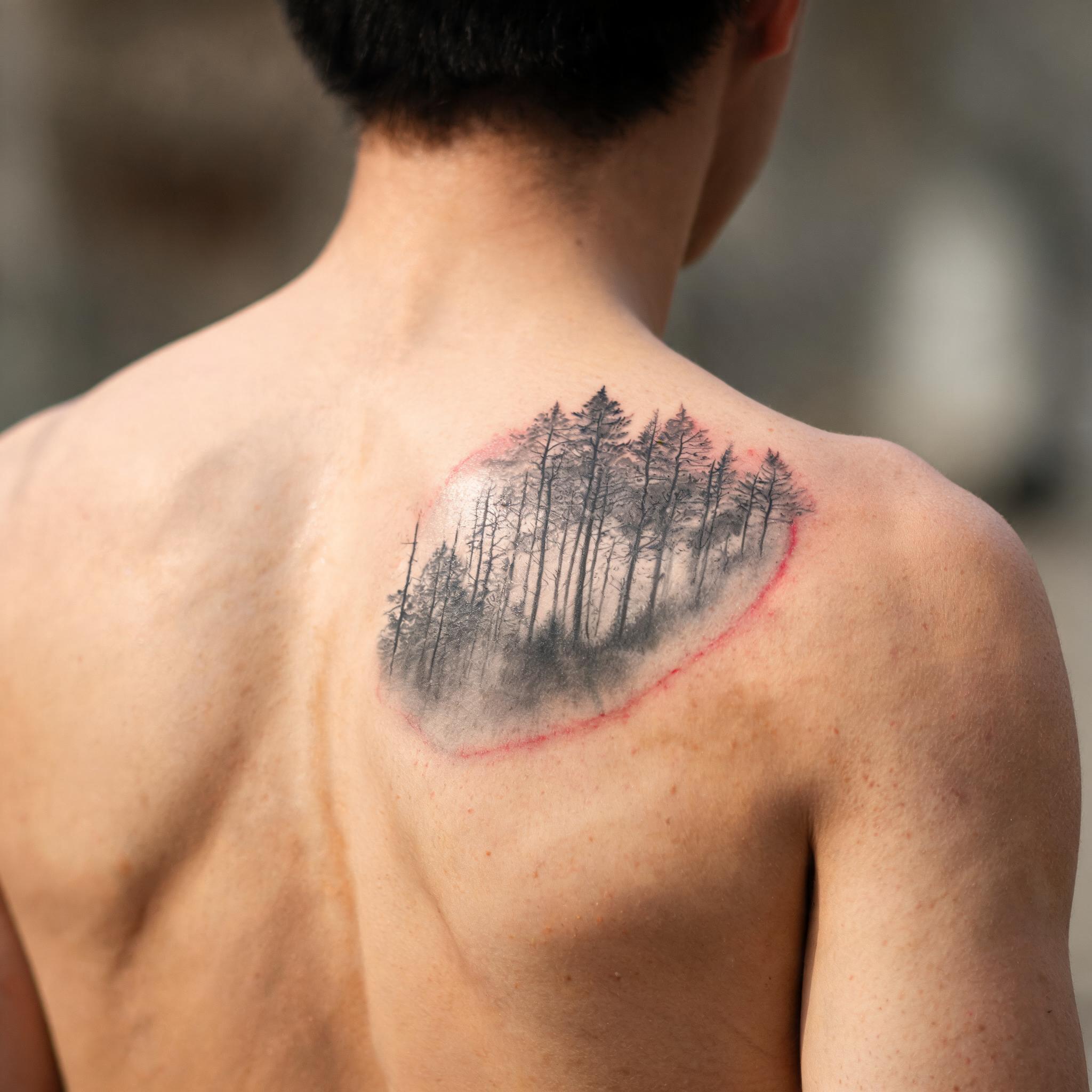Illustrative black-and-grey true image tattoo on a shoulder blade, shown in a soft-lit editorial tattoo photograph.
