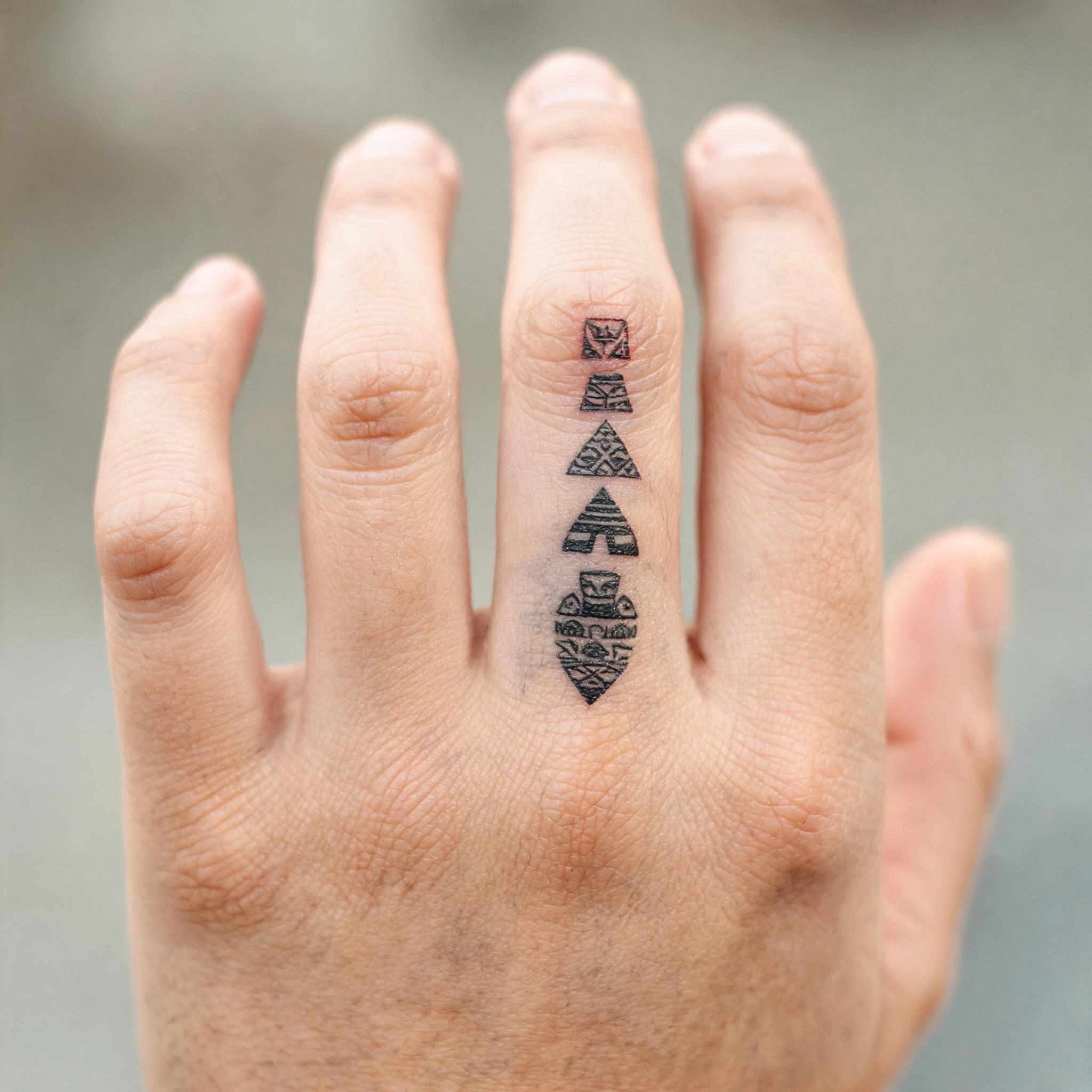 Aztec images tattoo in colour realism, shown on extended fingers against a white background, with lifelike shading and true-to-life tones.