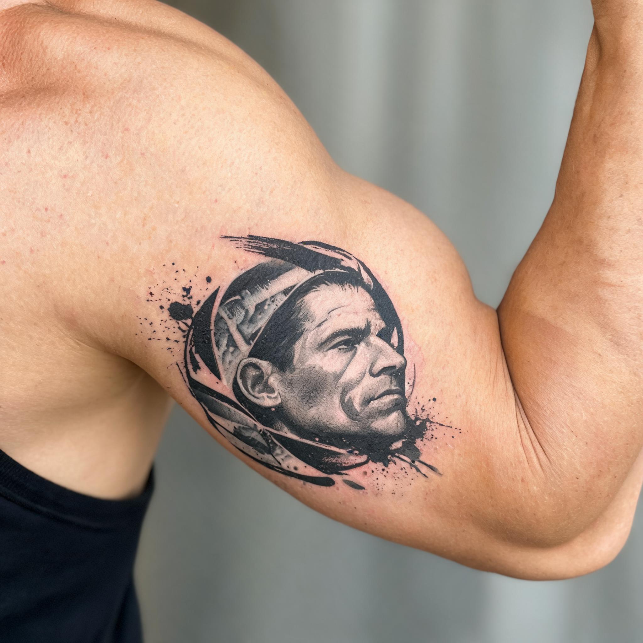 A trash polka tattoo image of a Pete Hegseth-inspired portrait on the inner bicep, shown on skin against a neutral background.
