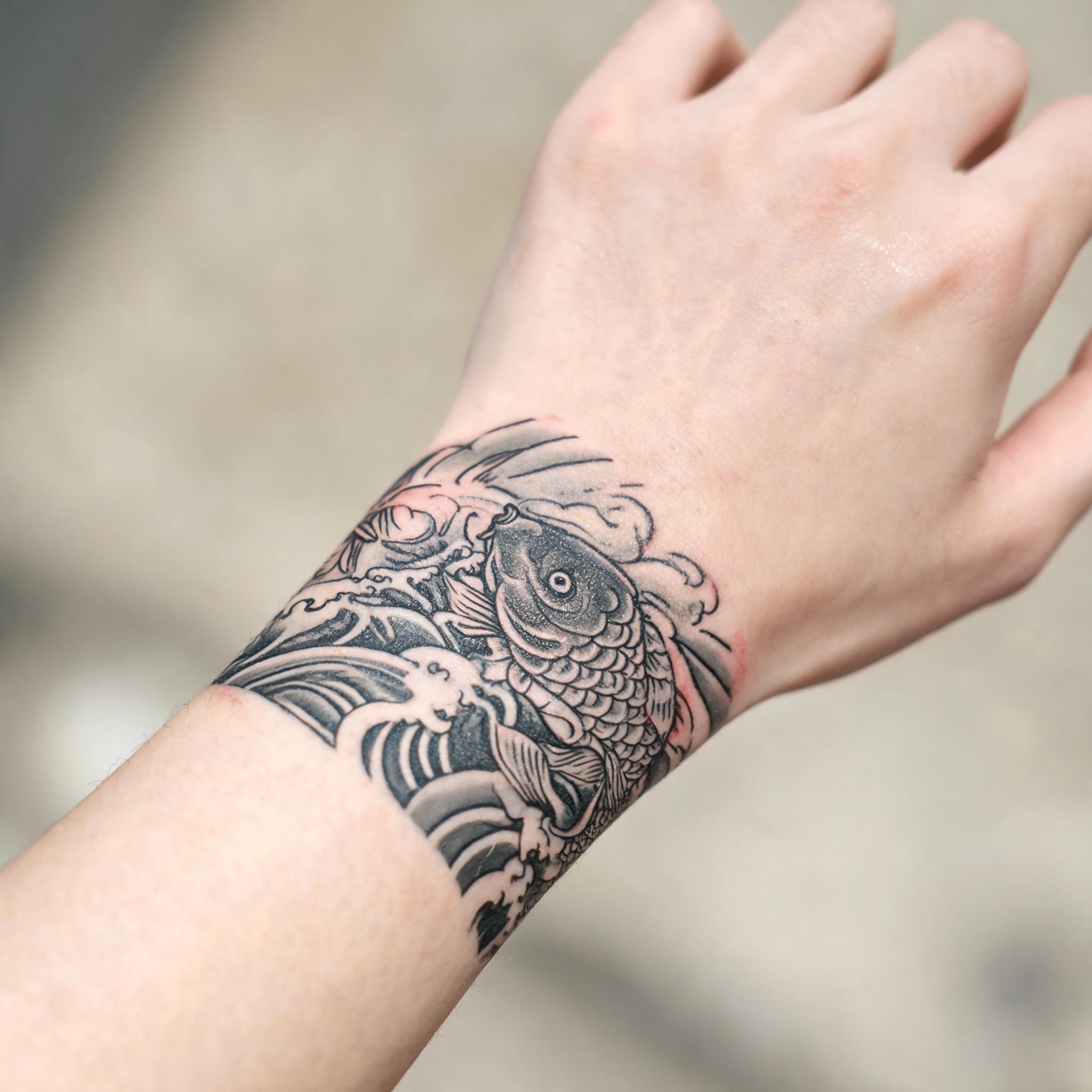 A Japanese irezumi samurai tattoo image on a wrist, black and grey ink with koi and waves, shown on a clean neutral background.