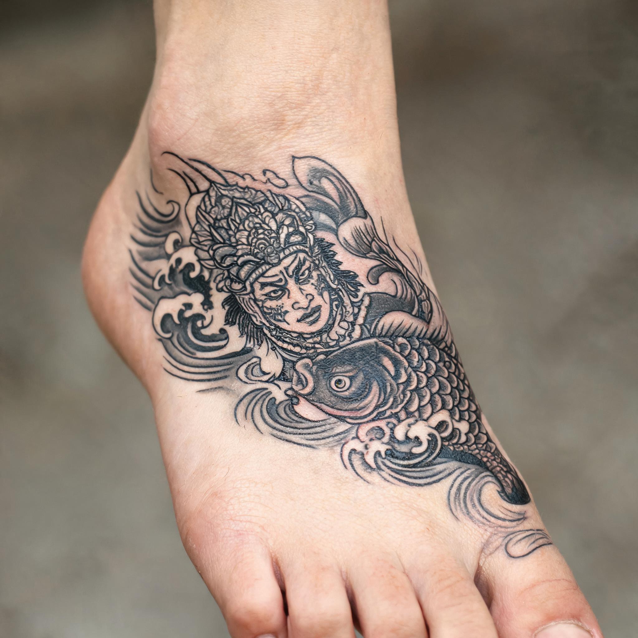 Aztec warrior tattoo image in Japanese irezumi style, black and grey, shown on the top of the foot against a clean neutral background.