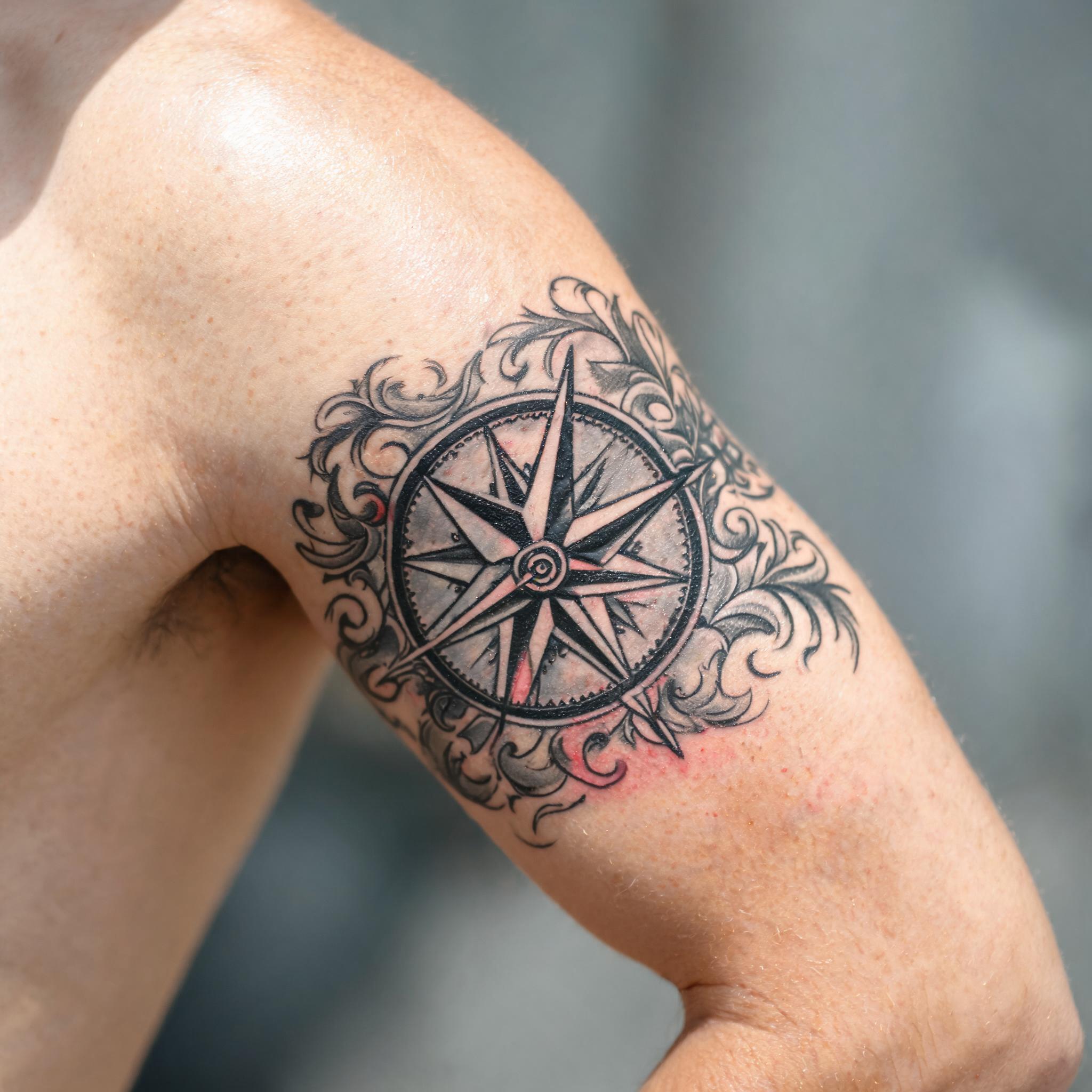 Neo-traditional nautical compass tattoo image on the outer upper arm, shown in black and grey on a clean neutral background.