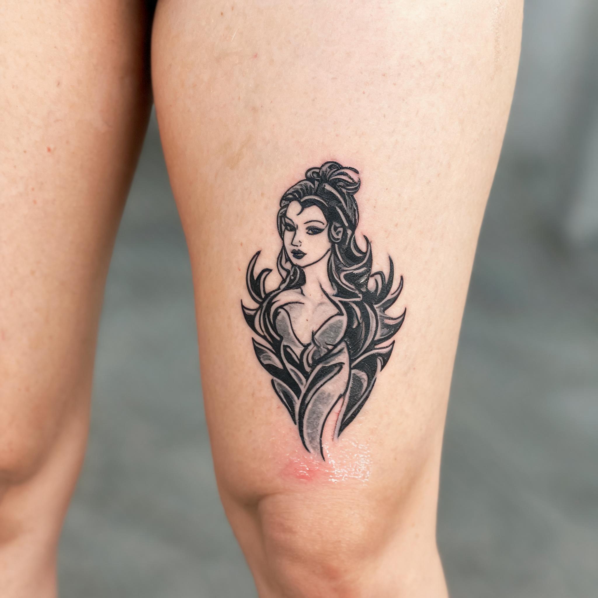 A female tribal tattoo image in American Traditional style, shown on the front thigh against a neutral background.