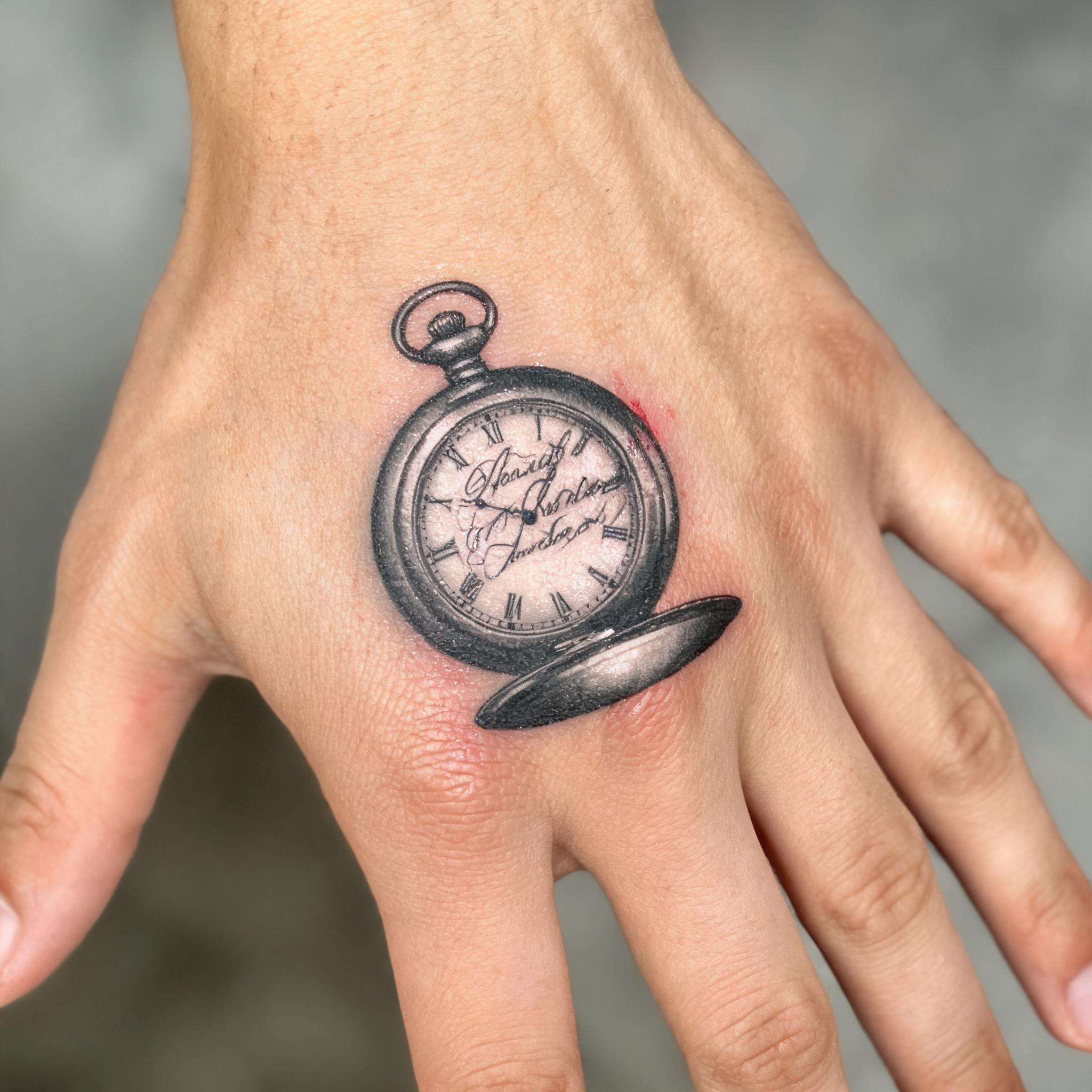 Tattoo image of a pocket watch rendered in elegant calligraphy script on the back of a hand, black and grey ink on white background.
