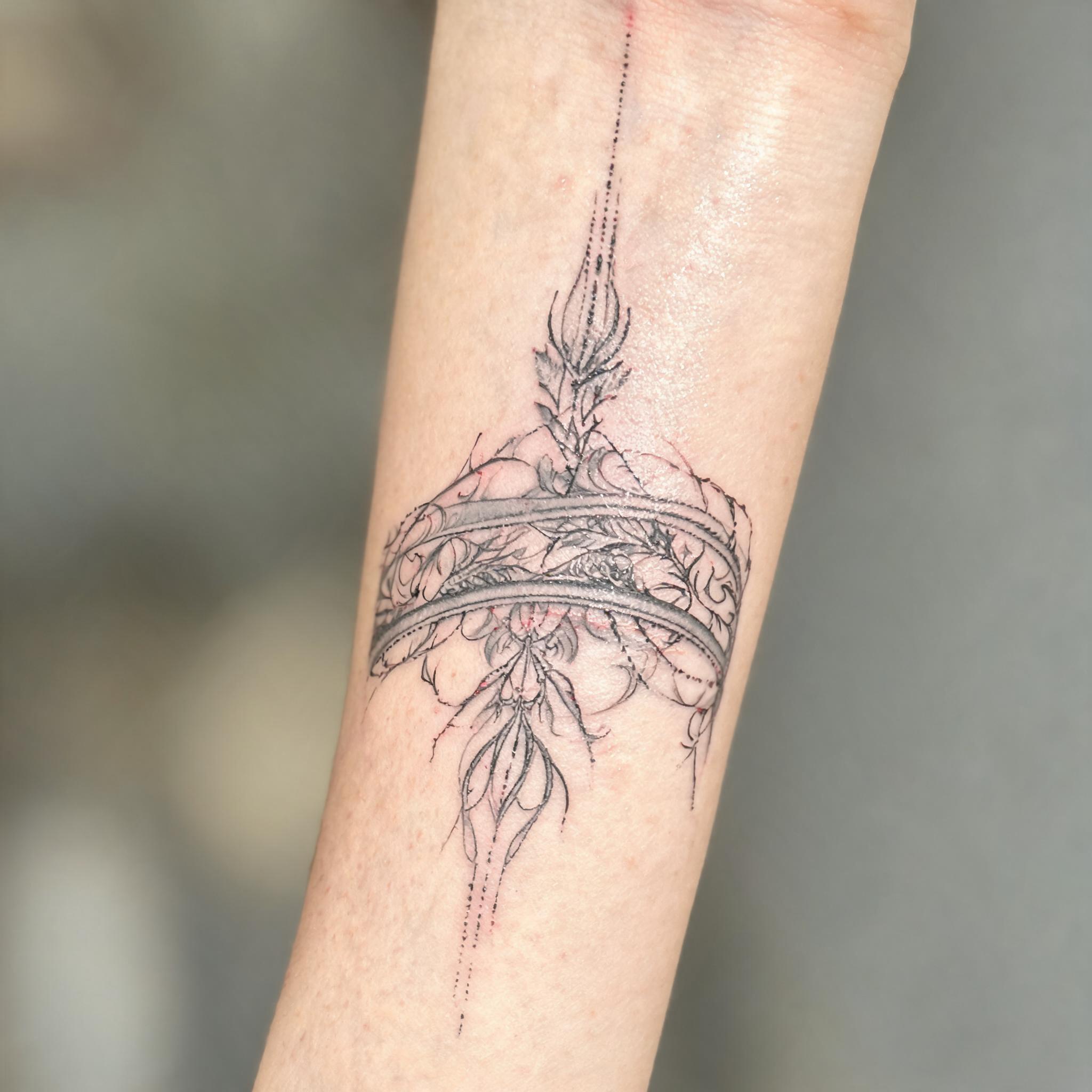 Fine line armband tattoo images on an inner forearm, black and grey single-needle work photographed on skin against a clean neutral background.