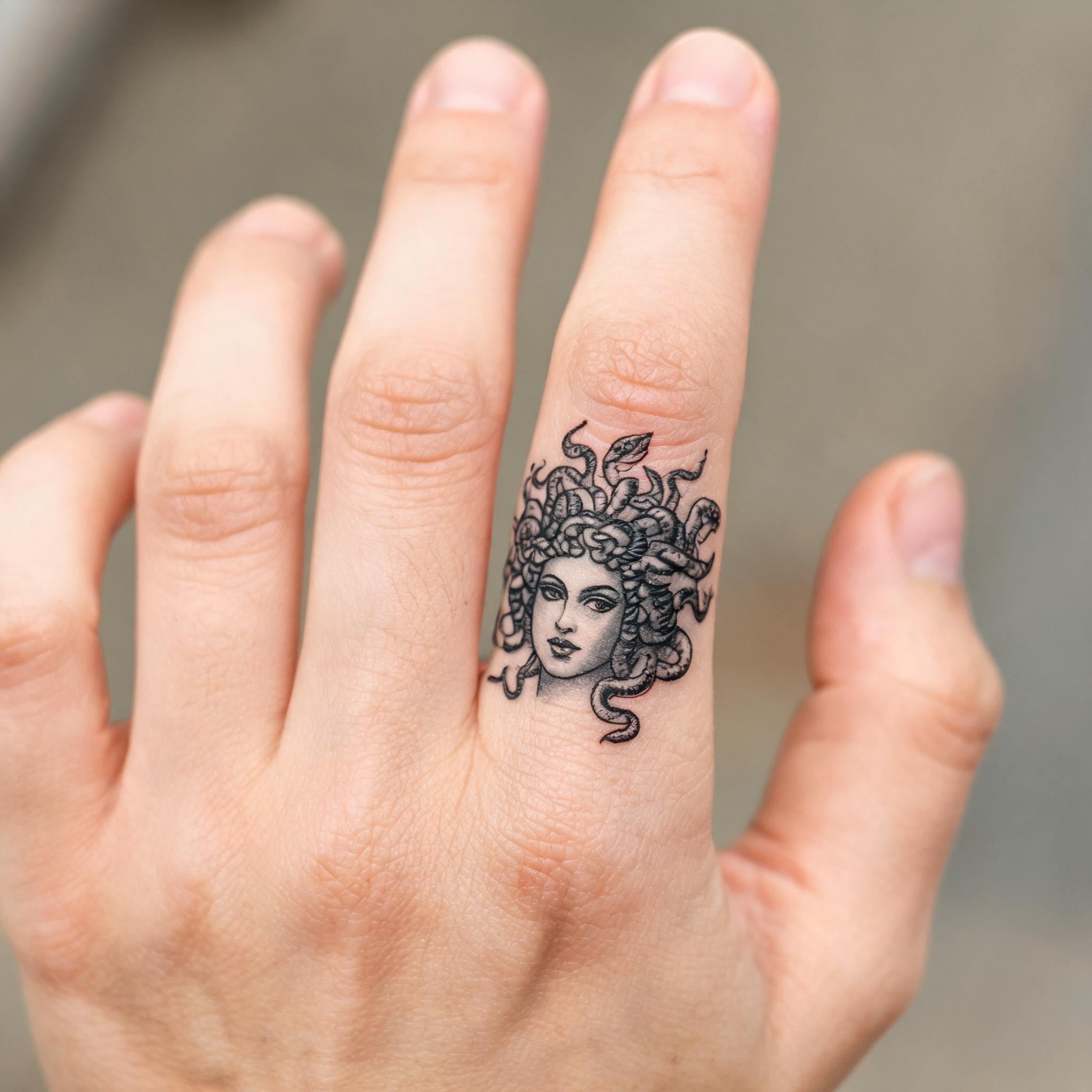 Blackwork Medusa tattoo design on a hand with extended fingers, shown against a neutral background as a tattoo image.