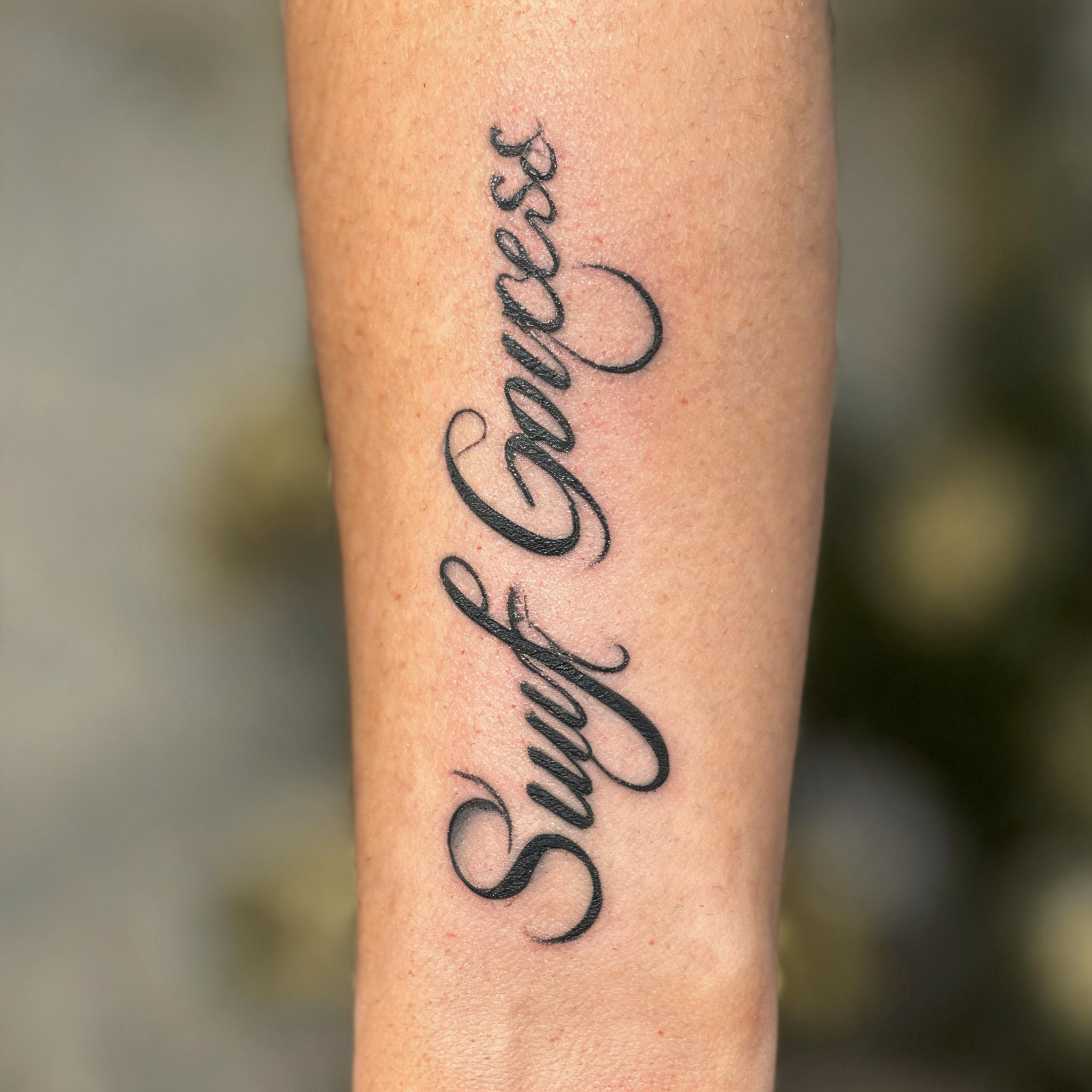 Egyptian goddess tattoo design in elegant calligraphy script on an outer forearm, black and grey ink, white-background tattoo image.