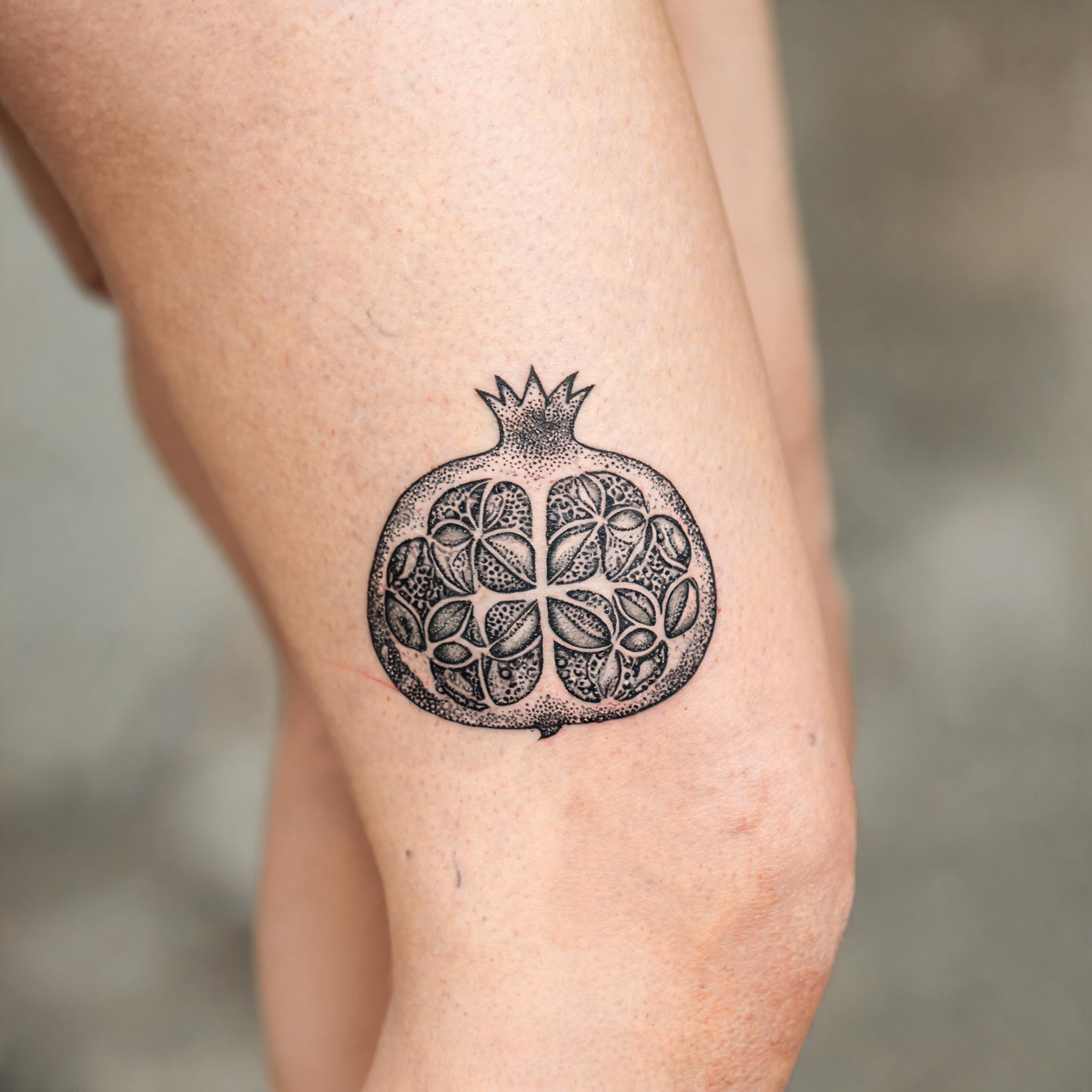 Geometric dotwork pomegranate tattoo design on the outer thigh, shown in black and grey ink on realistic skin against a plain background.