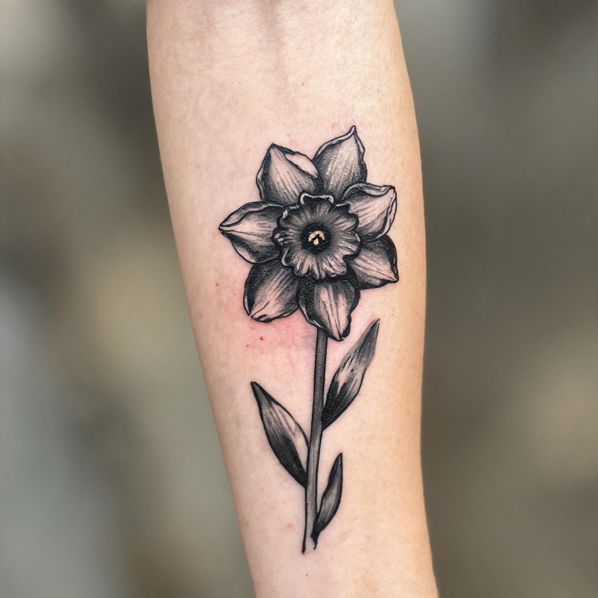 Blackwork daffodil tattoo image design on a person's outer forearm, shown in a close-up photo against a clean neutral background.