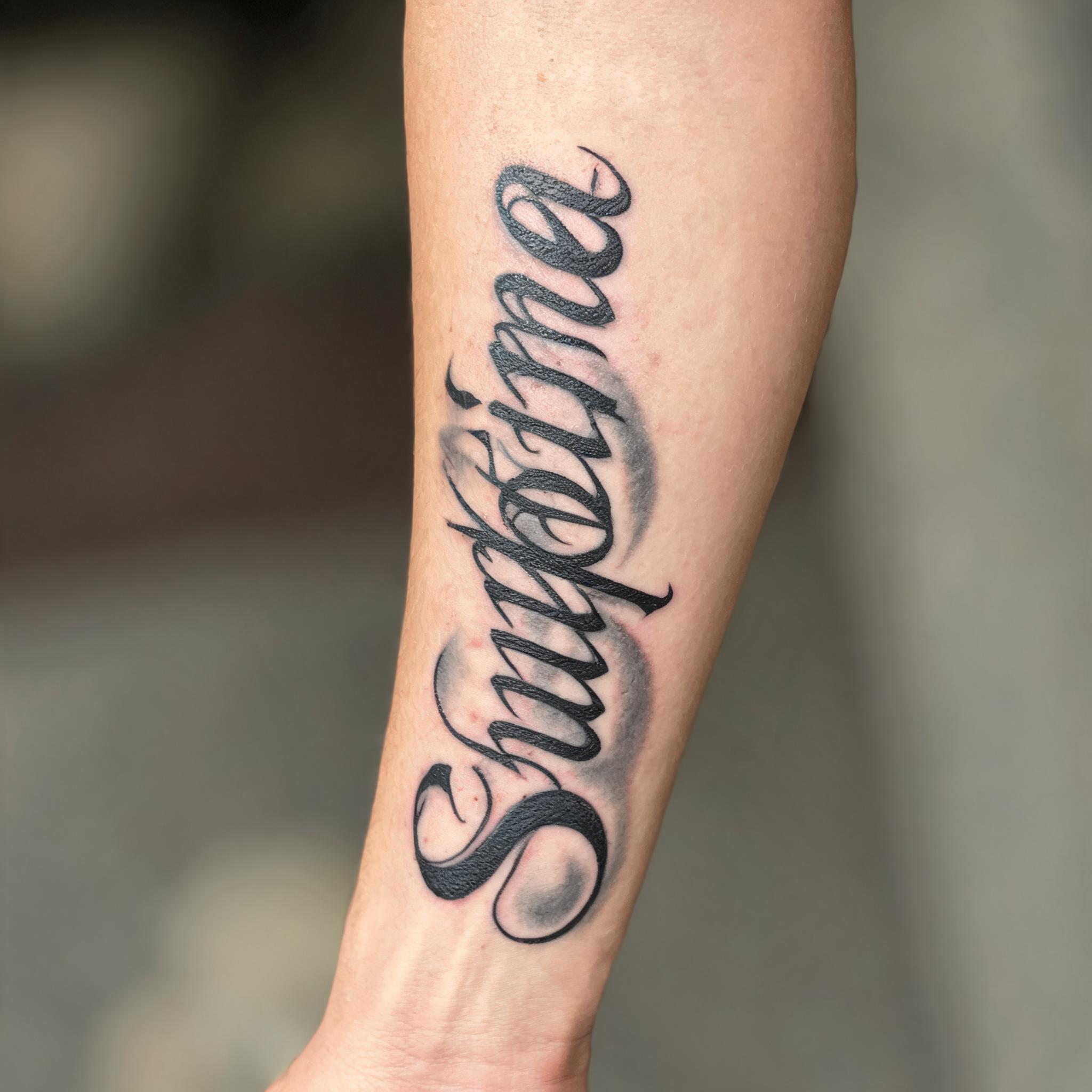 Chicano rose tattoo design in elegant script lettering on an outer forearm, black and grey ink on a white background, shown as a tattoo image.