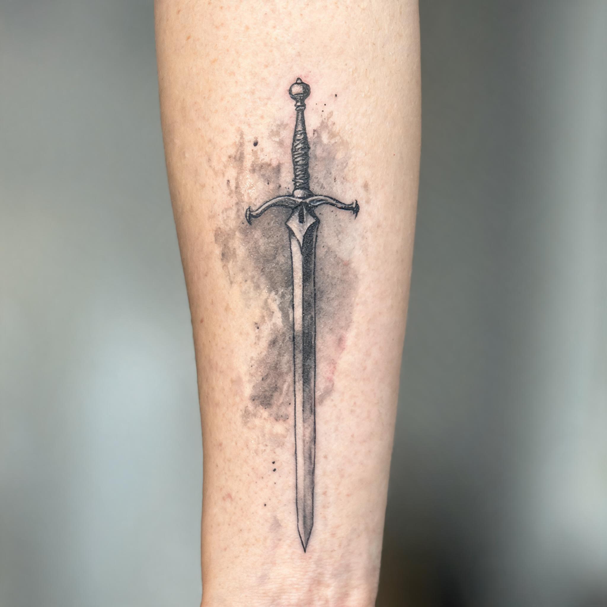 A medieval sword tattoo image design in watercolor style, shown on an outer forearm against a clean neutral background.