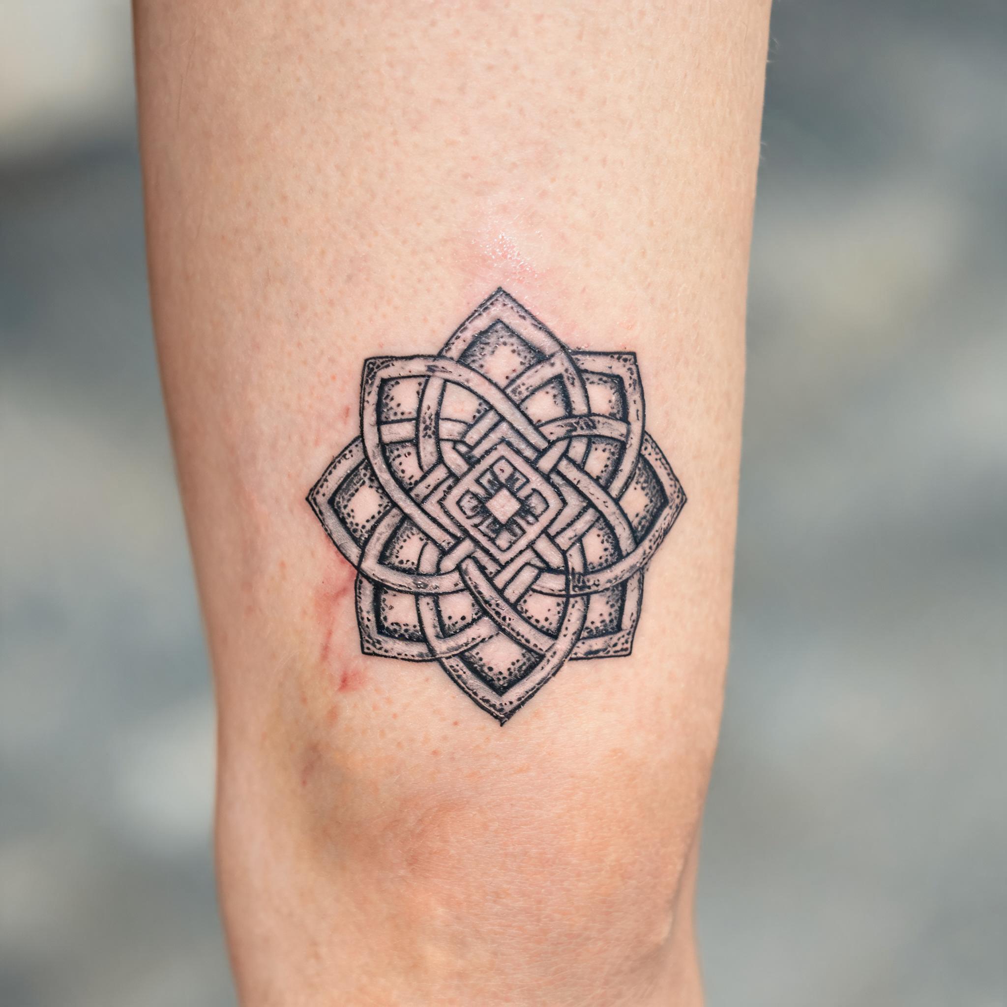 Black and grey Celtic knot tattoo design on a front thigh, shown as a geometric dotwork tattoo image against neutral skin.