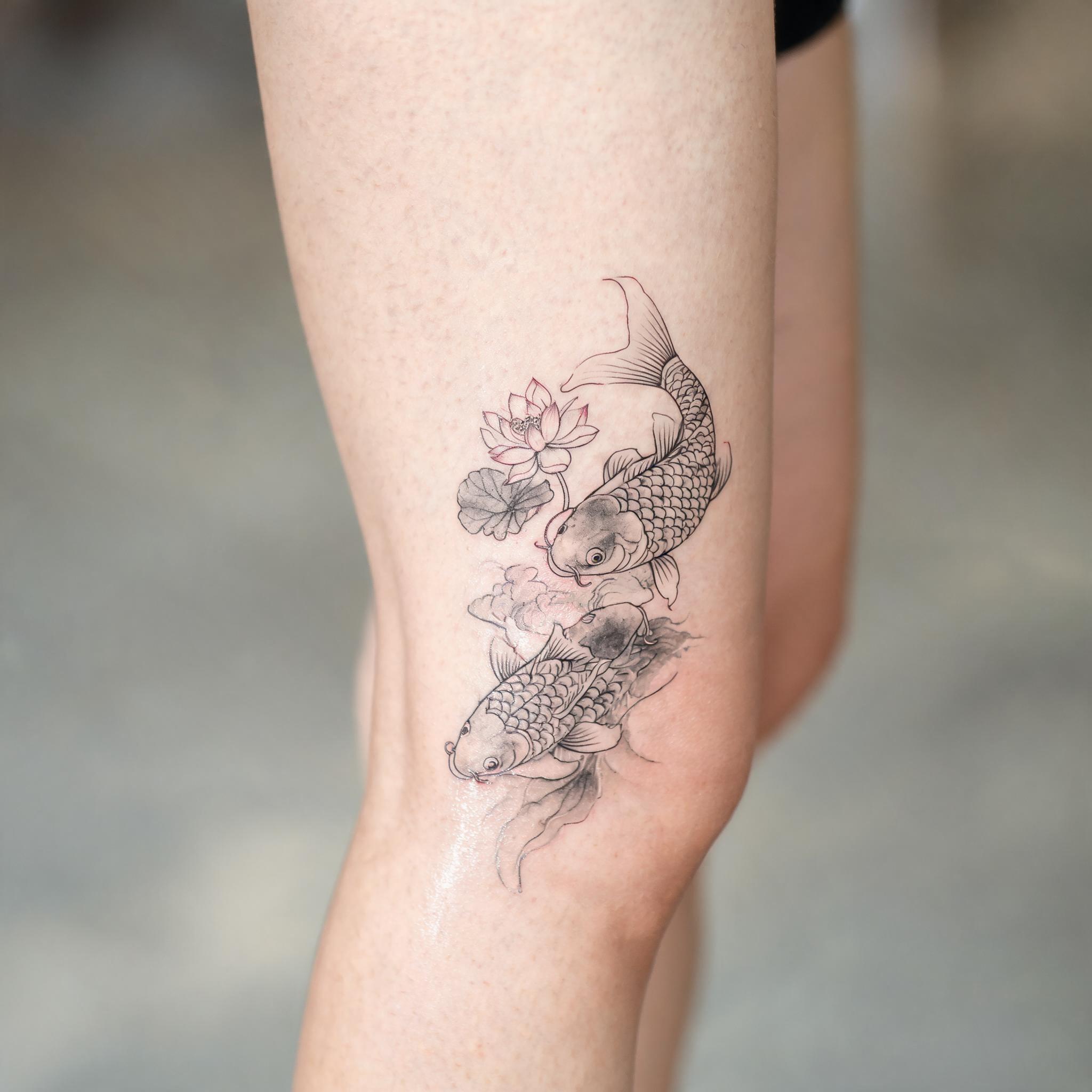 Fine line koi fish and lotus tattoo on a front thigh, delicate single-needle lines with soft greywash, shown on white.
