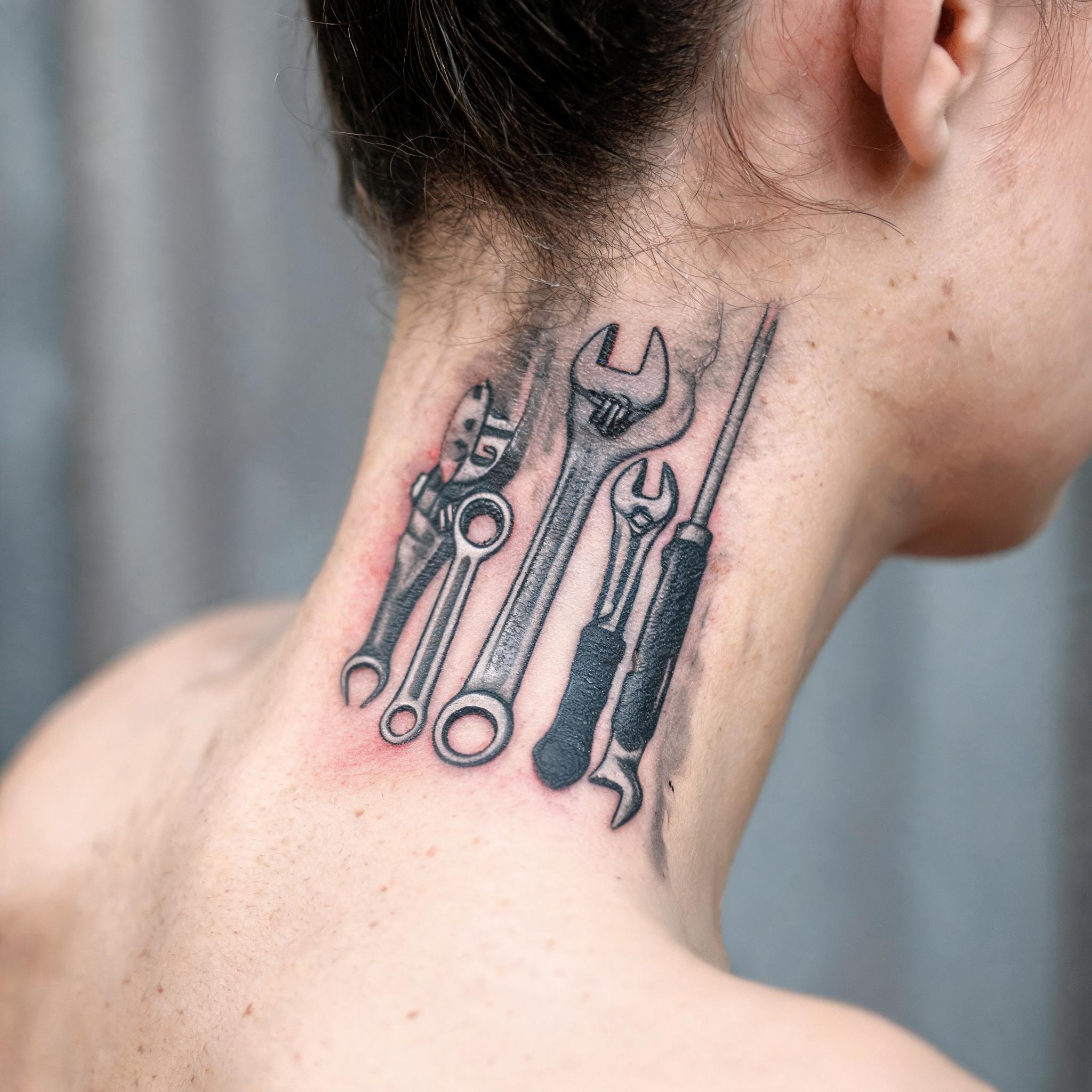 Black and grey realism tattoo of a mechanic tools design on the neck, shown on skin against a neutral background as a tattoo image.