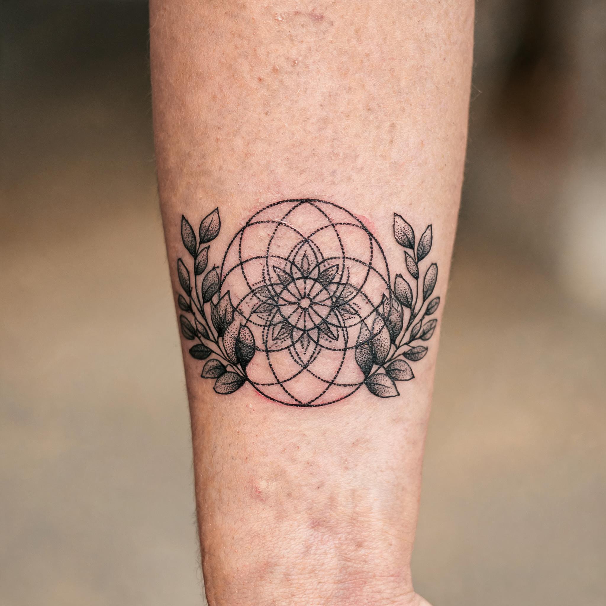 A black and grey eucalyptus branch tattoo image design in geometric dotwork, shown on an outer forearm against a neutral background.