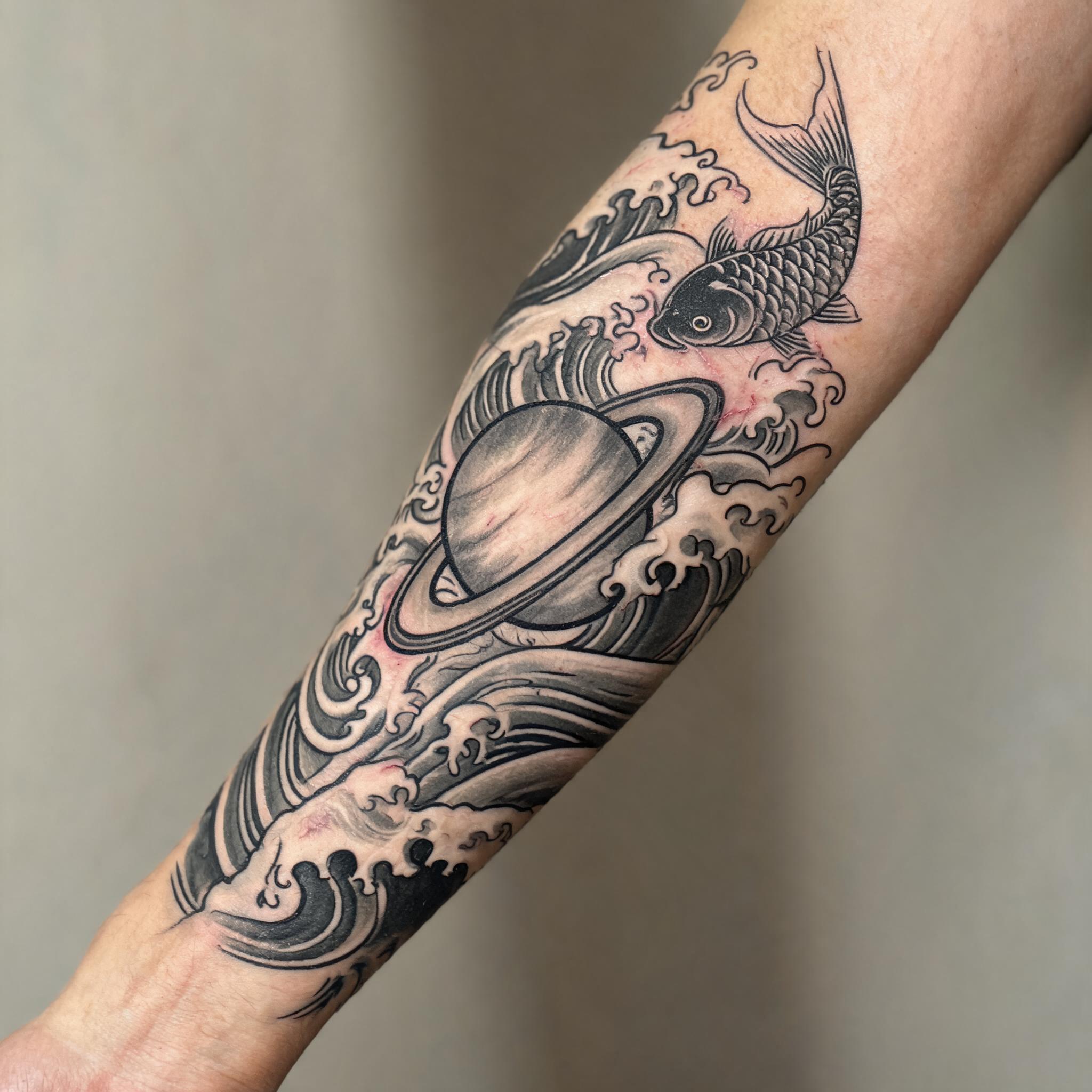 A black and grey Japanese irezumi Saturn planet tattoo image design on the outer forearm, shown on skin against a clean neutral background.