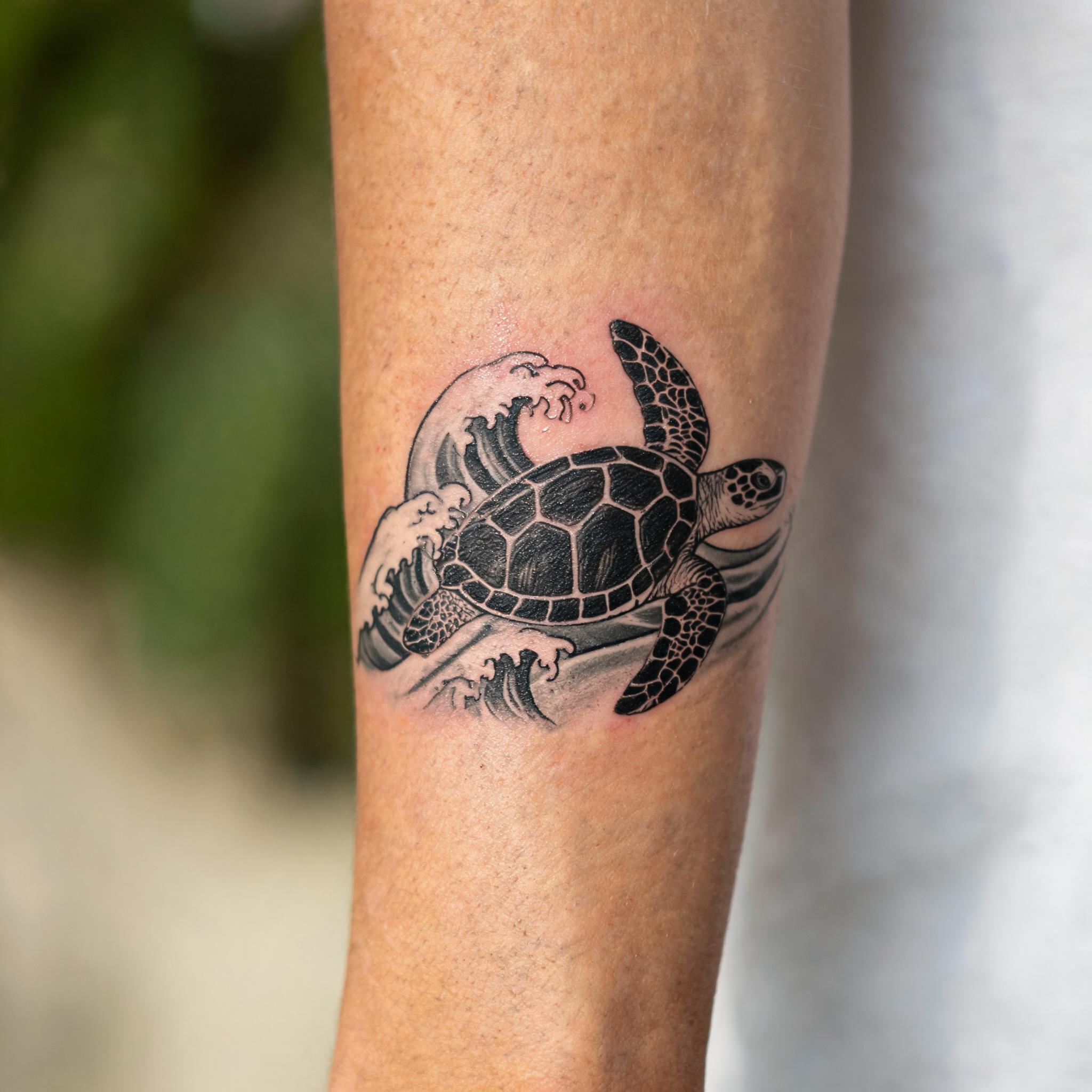 Blackwork sea turtle wave tattoo on an outer forearm, shown in high-contrast black and grey ink on a white background.