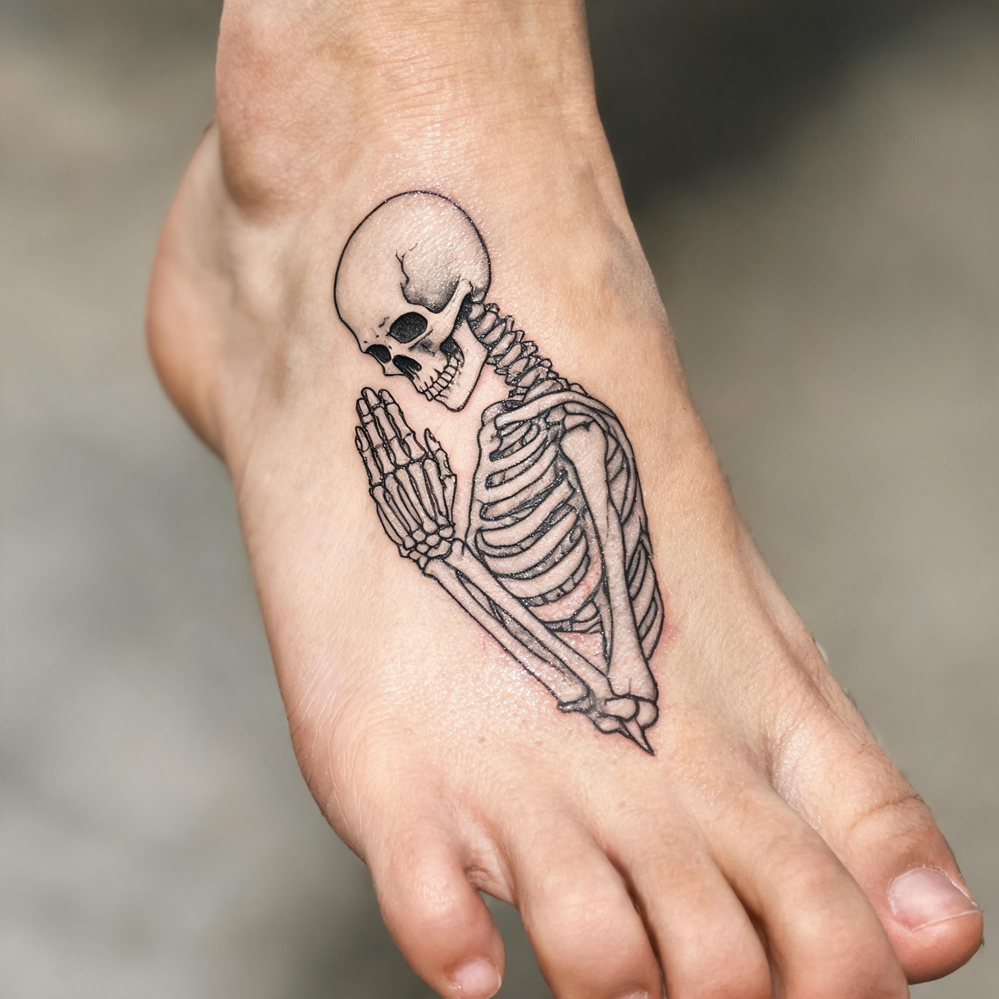 Fine line praying skeleton tattoo image design on the top of a foot, black and grey ink on realistic skin, photographed from above.