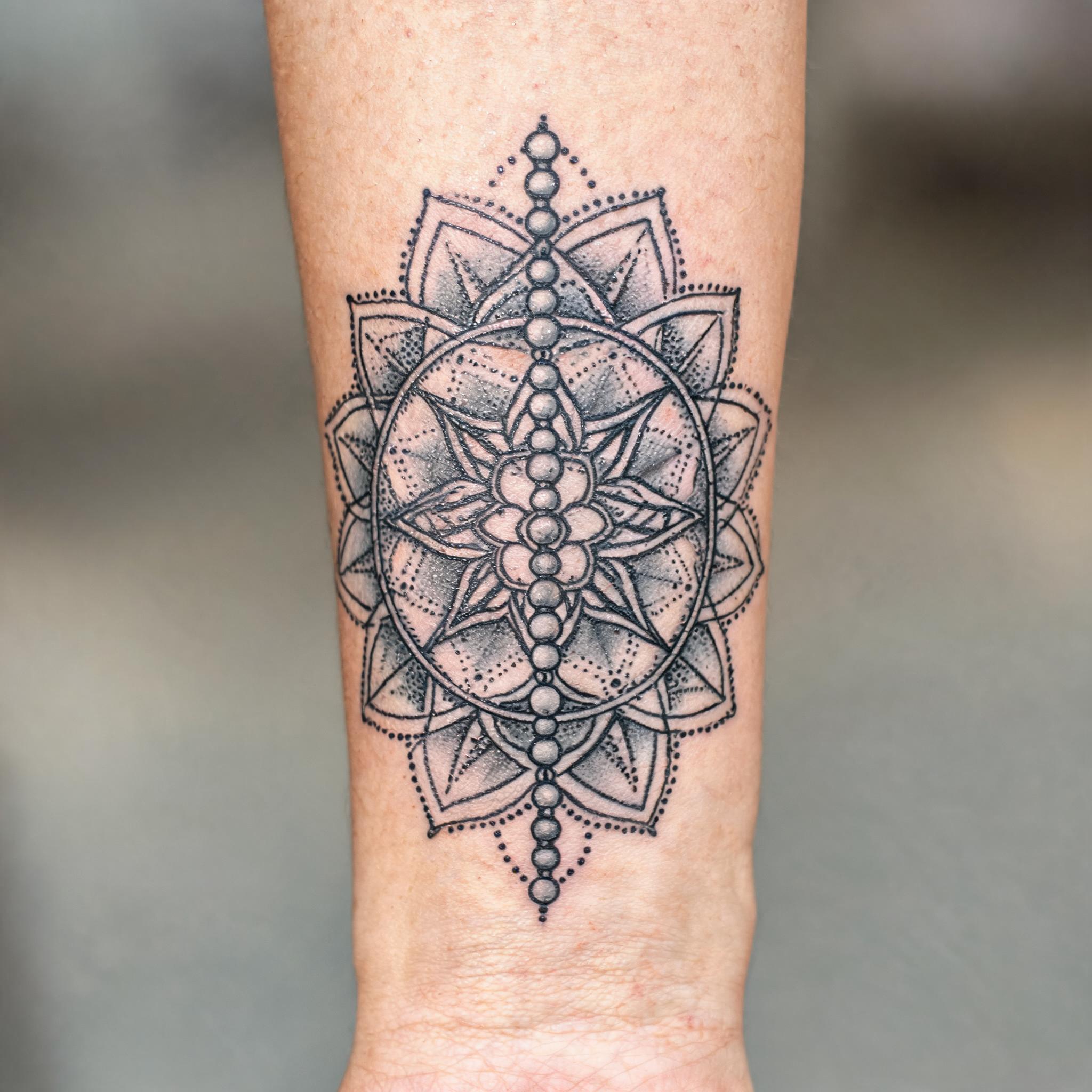 A black and grey geometric dotwork rosary beads tattoo image design shown on an inner forearm against a clean neutral background.