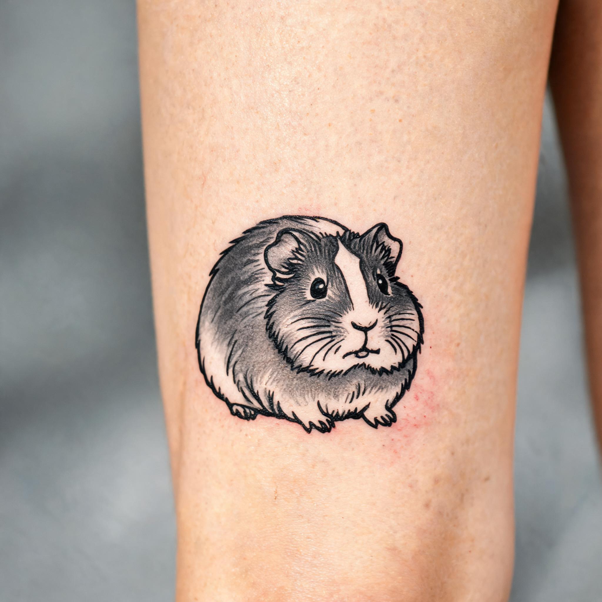 American traditional guinea pig tattoo image design on the front thigh, black and grey ink on skin against a clean neutral background.