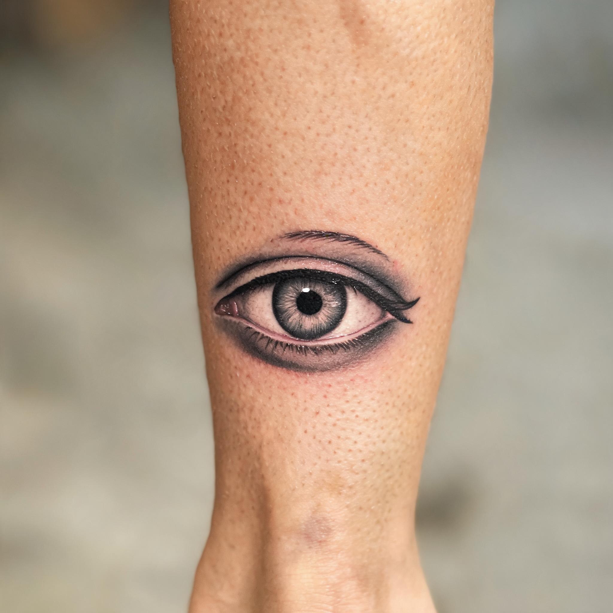 Black and grey realism third eye tattoo on a calf, shown as a tattoo image against a neutral background.