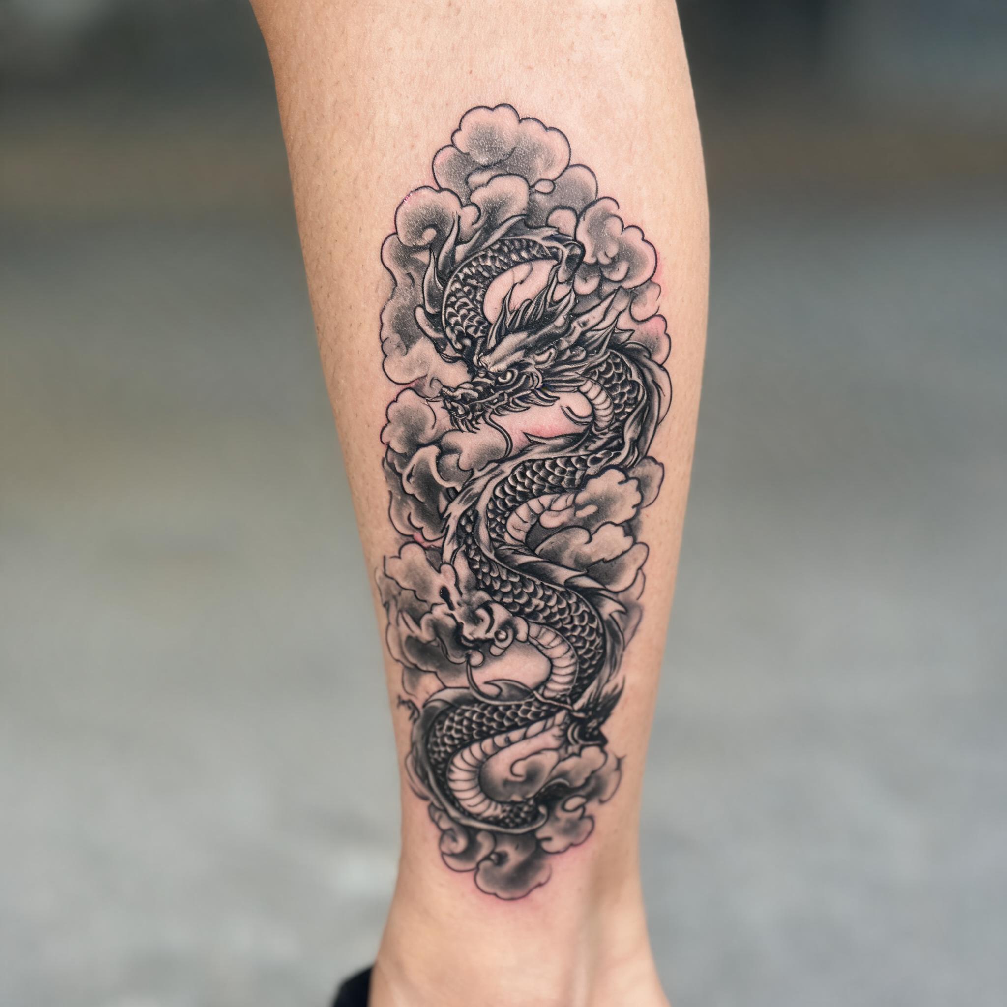 A black and grey neo-traditional Japanese dragon cloud tattoo on the shin, shown on realistic skin against a neutral background.