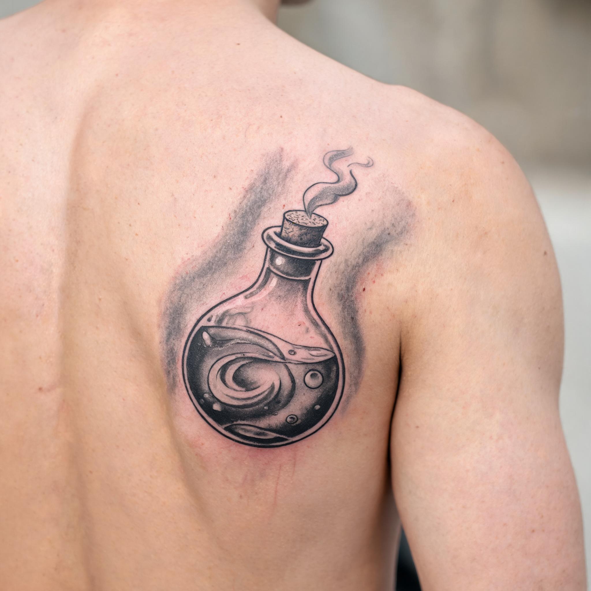 Black and grey witchy potion bottle tattoo on a shoulder blade, shown in soft daylight as a freshly inked tattoo image.