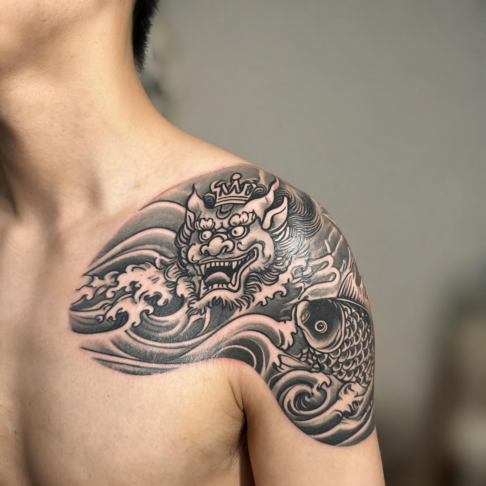Black and grey Japanese Irezumi lion crown tattoo on a shoulder cap, photographed close-up against a plain background.