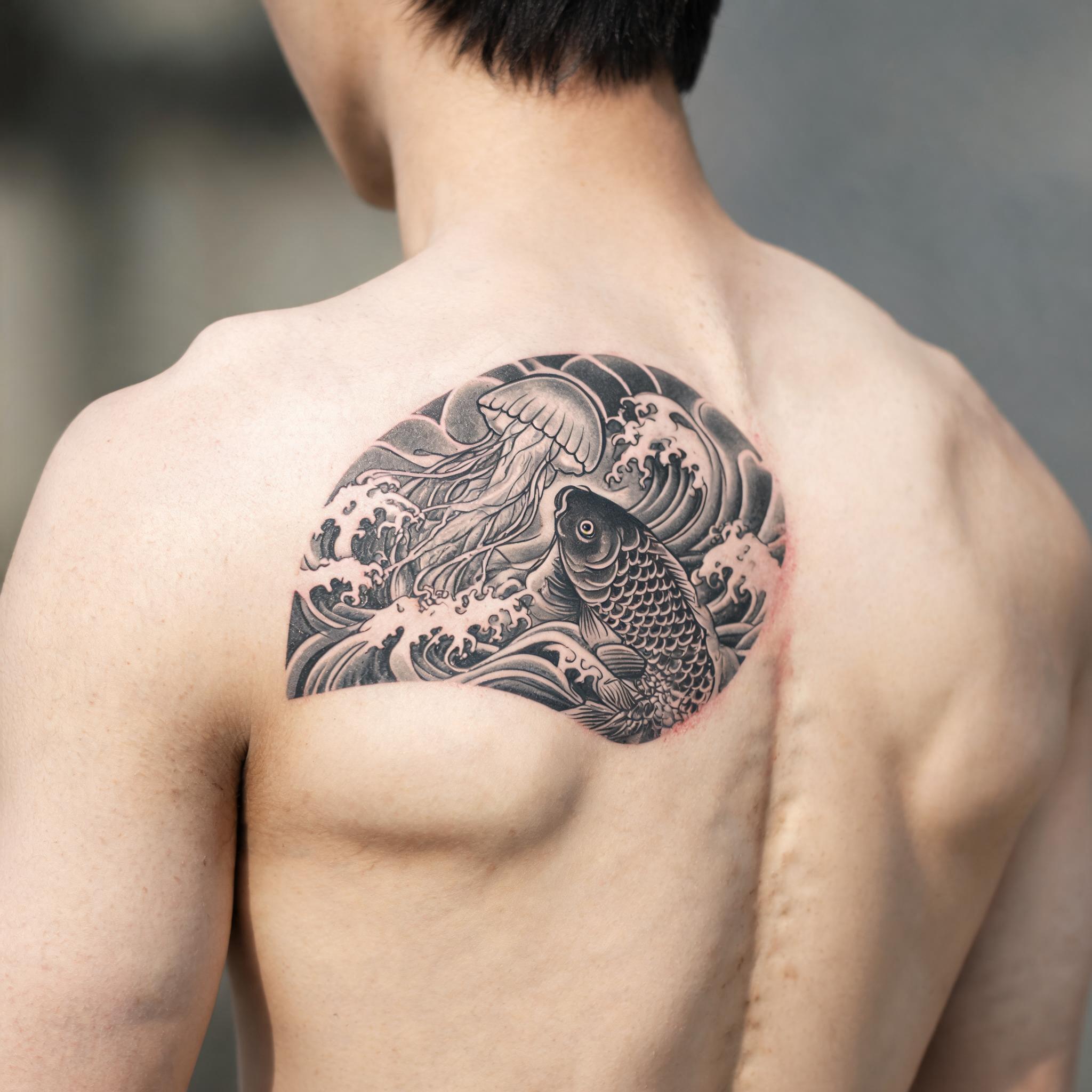 A fine line jellyfish tattoo design in Japanese irezumi style on a shoulder blade, shown in black and grey ink on natural skin.