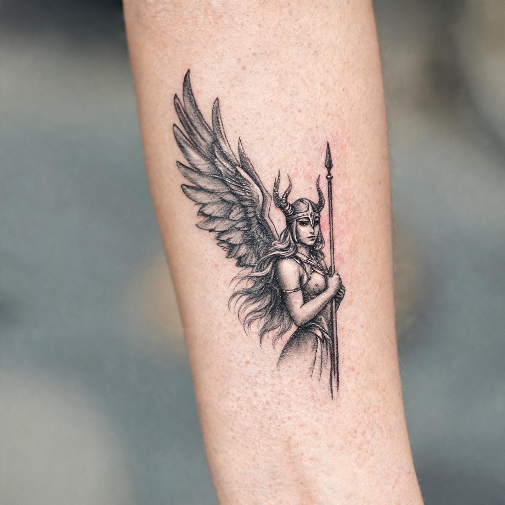 A Norse valkyrie tattoo image design in black-and-grey colour realism, shown on an inner forearm against a clean neutral background.