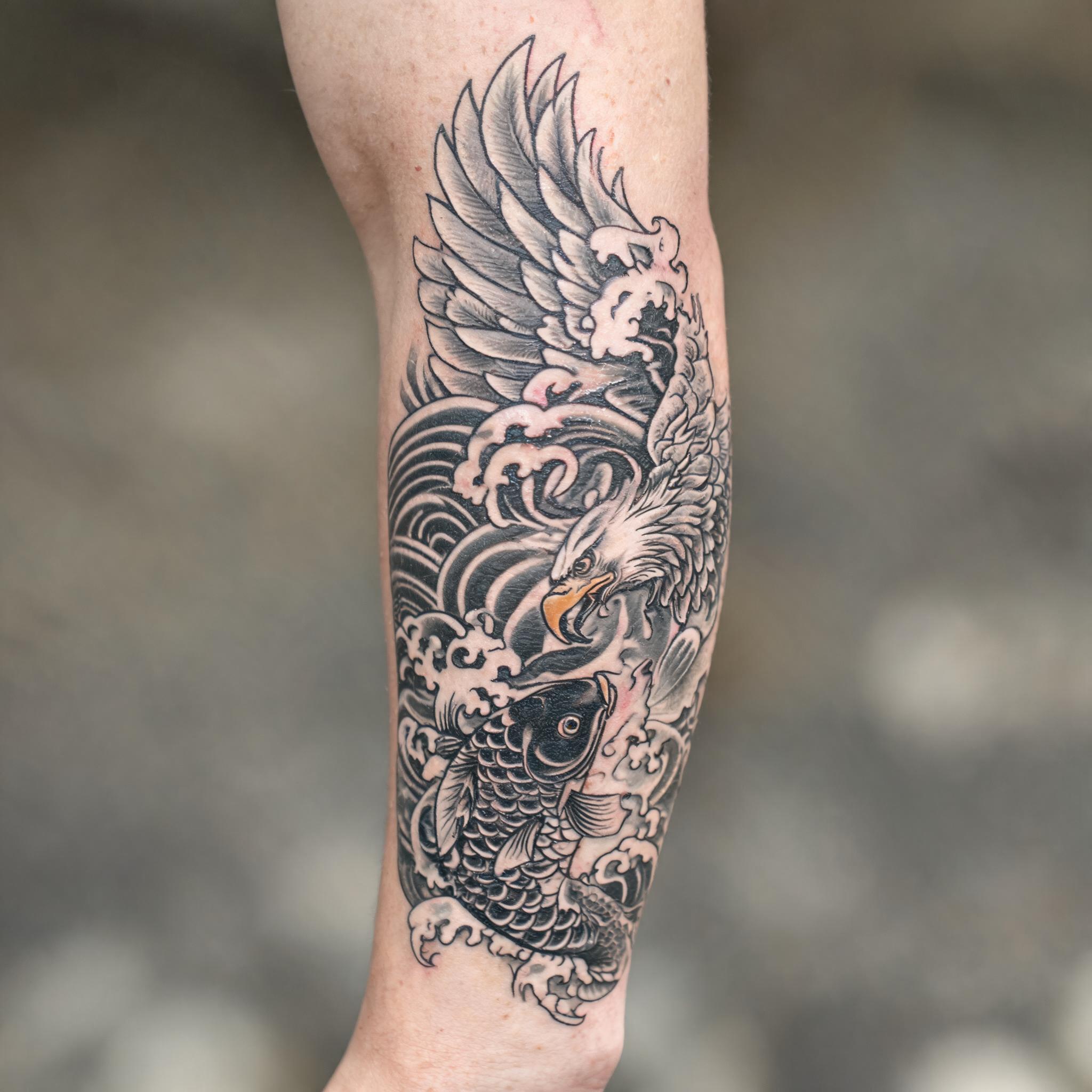 A black and grey Japanese irezumi bald eagle feather tattoo on an outer forearm, photographed on skin against a neutral background.