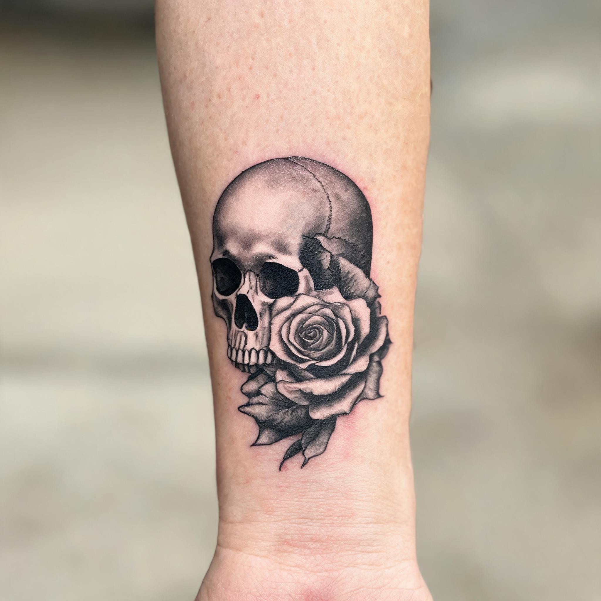 A tattoo image of a skull and rose design in colour realism, shown on an inner forearm against a clean neutral background.