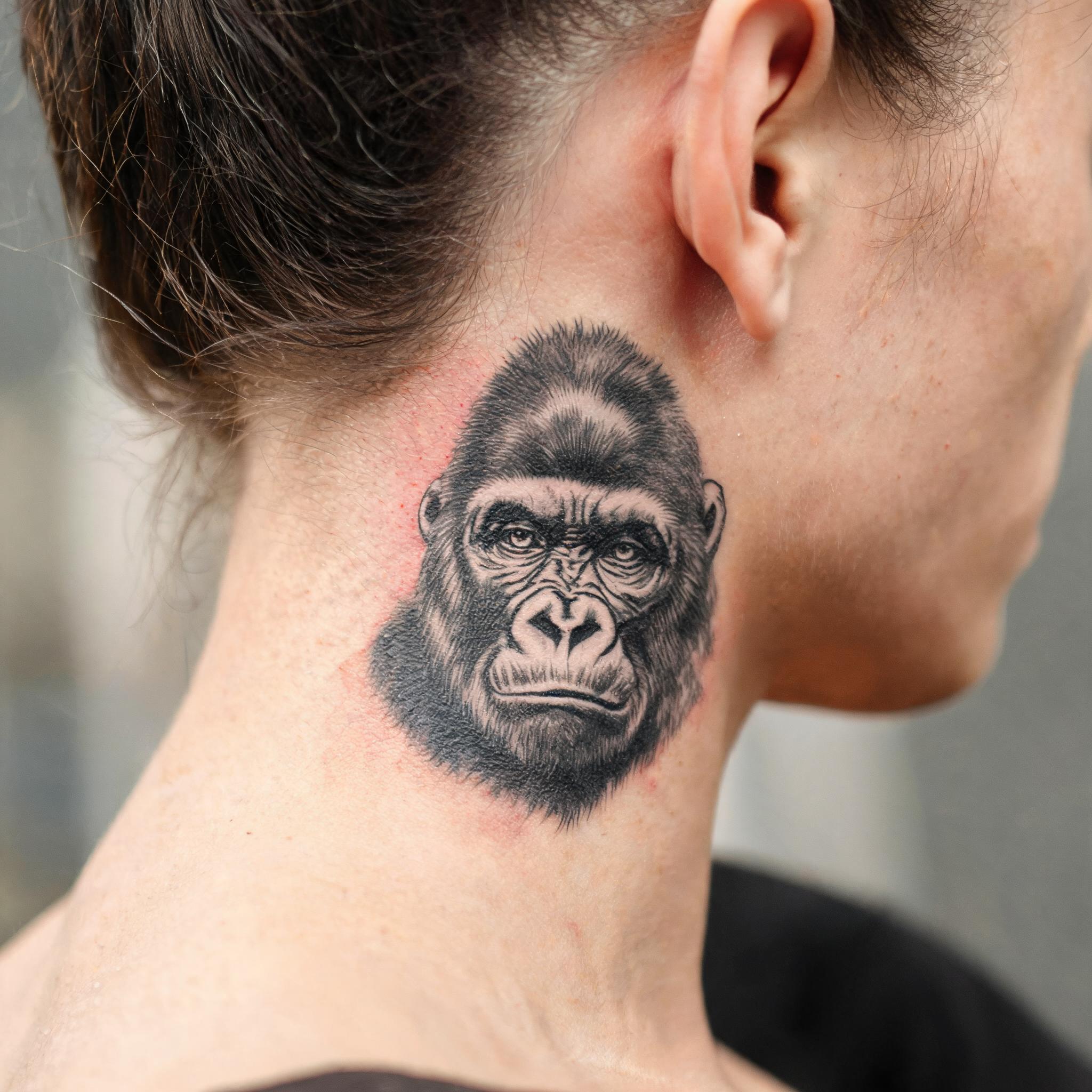 An illustrative black-and-grey gorilla tattoo image design inked on the nape of a neck, shown on natural skin against a plain background.